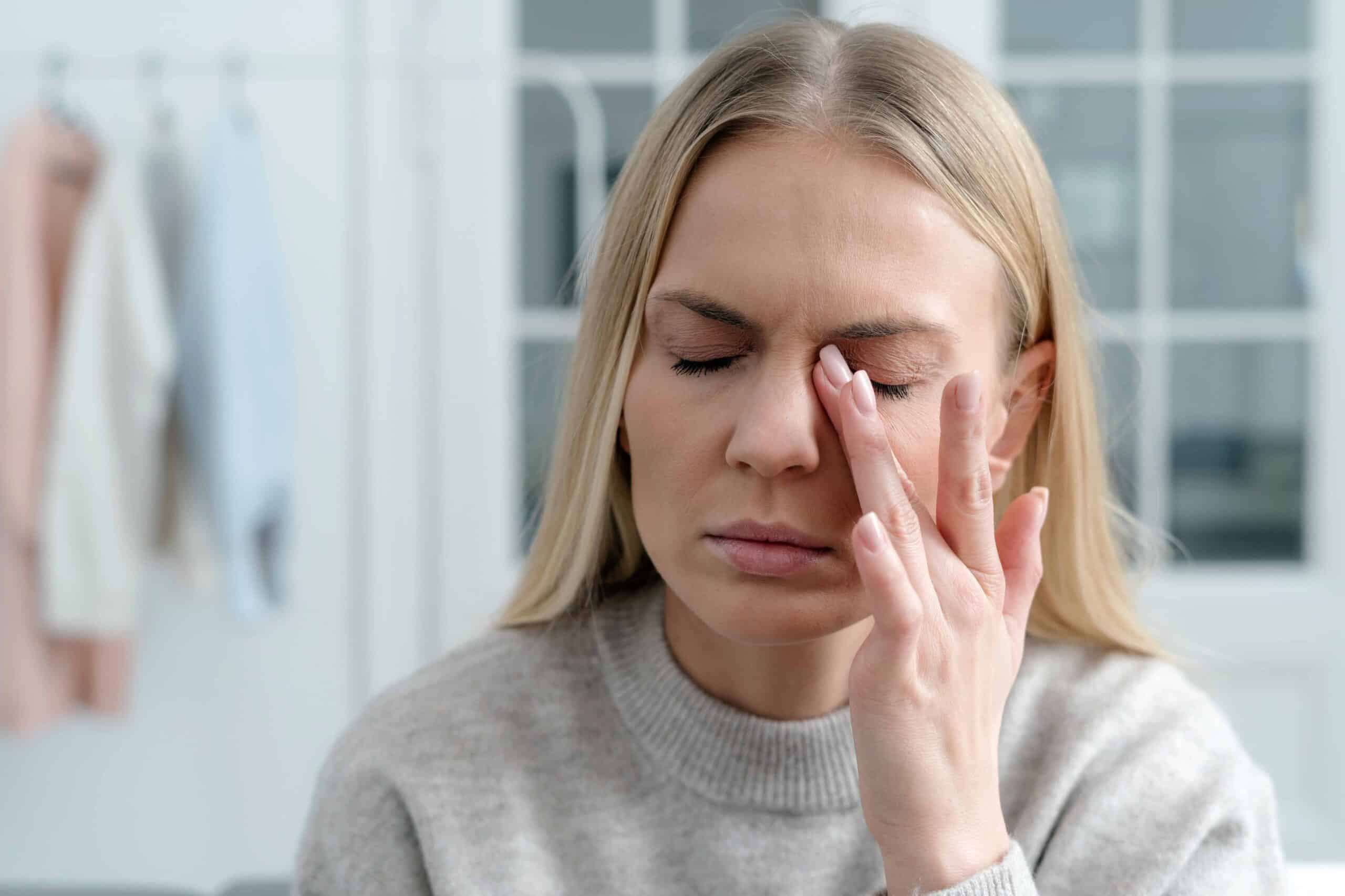 Eine blonde Frau reibt sich ihr linkes Auge.